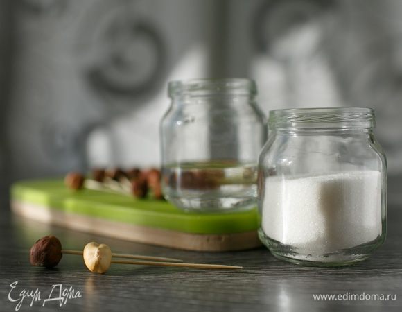 И последнее приготовление к решающему завтрашнему дню. Самое интересное. Целые ядра обжаренного фундука ТМ «Семушка» осторожно наденем на зубочистки. Соединим сахар (70 г) и воду (40 г) в алюминиевом ковшичке или в маленьком сотейнике с толстым дном, только не в эмалированном, поставим на огонь и будем варить карамель до красивого цвета. Уберем с огня, поставим кастрюльку на бочок, так как жидкости будет мало. Ждем, когда карамель начнет густеть. Теперь быстро берем орешек, окунаем в карамель, подвешиваем на изготовленное заранее устройство для сушки орешков в карамели. Делать все надо очень быстро, если карамель застыла, просто снова подогреть ее и быстренько продолжить. Чересчур длинные кончики подрезаем ножницами. Фотографии нет, так как процесс настолько увлекательный, что про фотоаппарат я совсем забыла.