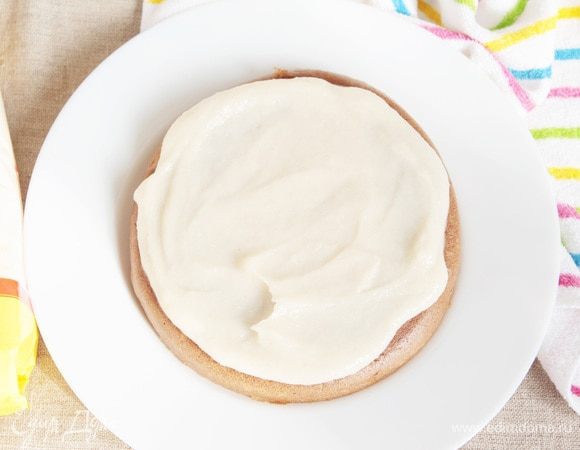 Светлый бисквит оставляем цельным. Выложить его на сервировочное блюдо дном вверх, полить сверху ложки 3–4 крема.