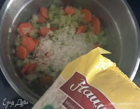 Пассеруем овощи до золотистого цвета. Всыпаем в кастрюльку Отборный рис ТМ «Националь». Перемешиваем, даем рису пару минут пропитаться маслом, ароматами овощей и орегано.