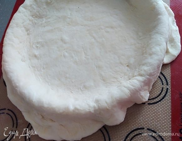 Нам понадобится форма для выпечки размером около 24–26 см. Смазать ее тонким слоем масла. Тесто раскатать на припыленной мукой доске. Поместить раскатанное тесто в форму так, чтобы края свисали.