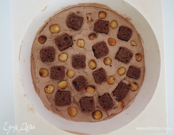 Равномерно распределить кубики шоколадного бисквита и обжаренный фундук, вдавливая их в ганаш, заморозить в морозилке до твердого состояния для удобства сборки.