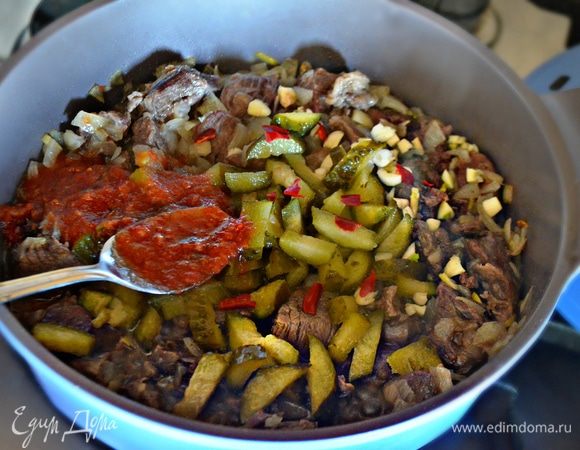 На растительном масле слегка обжарить нарезанный репчатый лук, добавить мясо и обжаривать в течение 10 мин, перемешивая. Затем добавить томатный соус (можно заменить 2 ст. л. томатной пасты, разведенной в кипяченой воде), нарезанные соленые огурцы, чеснок, слегка посолить и добавить сухие специи и небольшие кусочки жгучего перца (без семян!). Тушить около 10 мин.