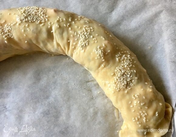 Также с помощью полотенца перенести штрудель на противень, выстеленный пергаментом для выпечки. В мисочку разбить два перепелиных яичка, разболтать вилочкой и смазать поверхность штруделя. А сверху присыпать семенами кунжута.