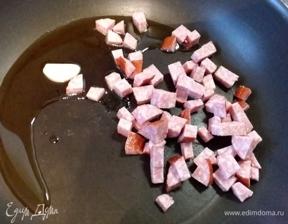 На сковороде разогреть оливковое масло, обжарить в нем зубчик чеснока, убрать его и выложить мелким кубиком нарезанные колбаски. Обжарить в течение нескольких минут до золотистого цвета. Убрать с огня.