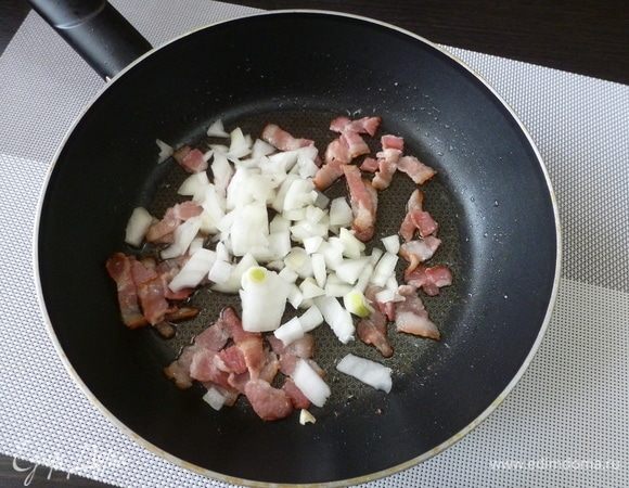 Полоски бекона нарезать кусочками поперек, обжарить на сковороде. Добавить нарезанный лук и обжарить все вместе.