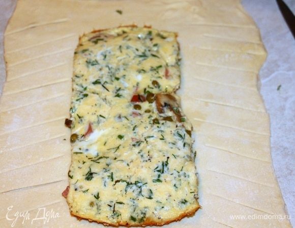 Тесто раскатать, на середину выложить яичницу, края теста надрезать на полосы.