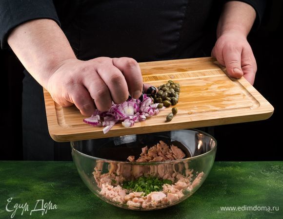 Добавьте к тунцу лук, петрушку, маслины и каперсы. Все перемешайте.