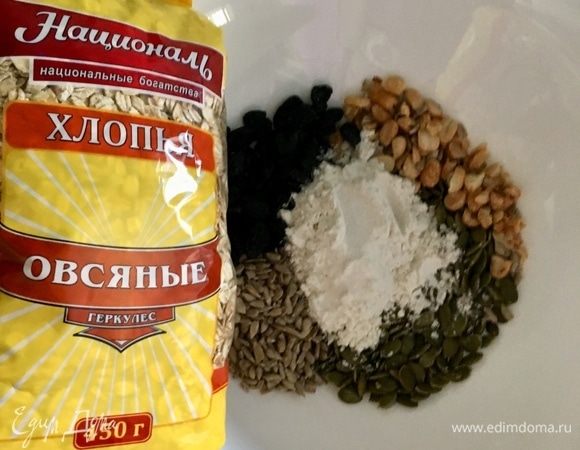 В миске соединяем два вида семечек, изюм, немного измельченные орехи и муку со щепоткой соли. По поводу муки. Вообще в данном рецепте рекомендуется использовать любую цельнозерновую муку, что, собственно, я и указала в ингредиентах. Сама же использовала муку универсальную без глютена. Просто в списке видов муки такой не нашлось. Теперь самое время отмерить 120 г овсяных хлопьев и добавить к остальным ингредиентам. Я еще немного смолола овсяные хлопья на пульсирующих движениях блендера (не стала фотографировать этот шаг).