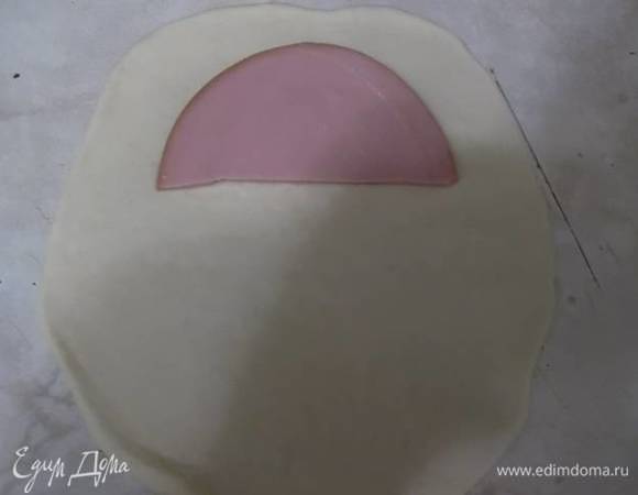 Тонко раскатываем тесто. Выкладываем половинку куска колбасы.