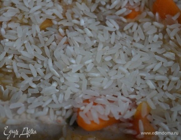 Когда мясо с овощами обжарились, всыпьте сверху пару горстей риса, налейте два стакана кипятка.