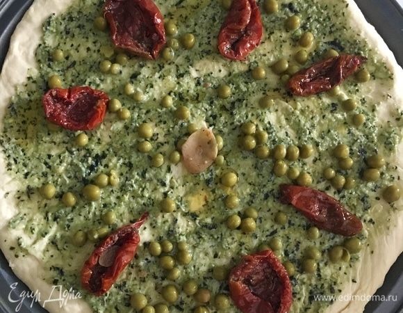Раскатать тесто в круг по диаметру формы. Но тонко можно не раскатывать. Тогда получим пышную лепешку с воздушным мякишем! Смазать пласт сначала соусом песто. Щедро смазать — получится только вкуснее. Выложить вяленые помидорки по кругу. Посыпать вкусным сладким горошком ТМ «Фрау Марта».