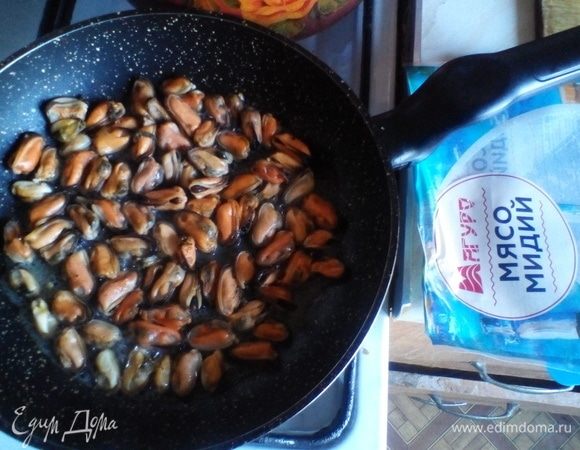Тем временем половину упаковки мяса мидий помещаем на разогретую противопригарную сковородку под крышку на медленный огонь. После того как мидии разойдутся и выделят сок, солим, добавляем молотый белый перец и оставляем томиться под крышкой минут на 10.