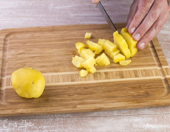 Сварите картофель в мундире, очистите от кожуры и нарежьте мелким кубиком.