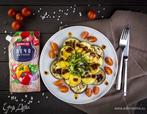 Выложите теплые овощи на блюдо слоями, полейте томатным соусом. Украсьте салат четвертинками черри и листьями руколы.