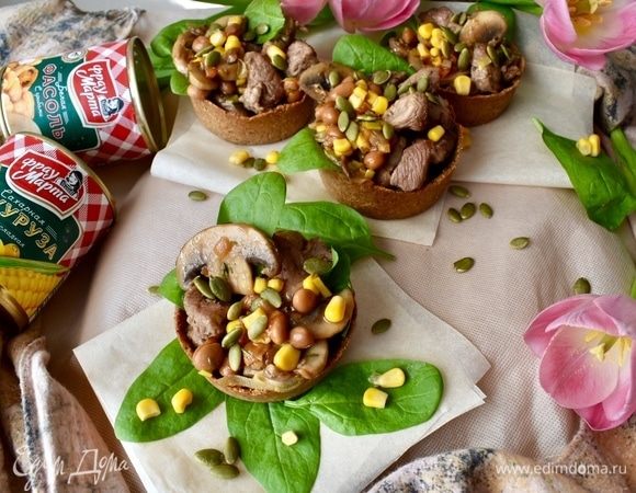 В каждую тарталетку кладем сперва сочный шпинат. Далее я распределила мясо индейки на четыре порции. Причем с овощами не перемешивала, а положила с одной стороны тарталети мясо. А с другой — овощной салат из грибов, белой фасоли и кукурузы. Ну, а сверху не забыть посыпать тыквенными семечками.