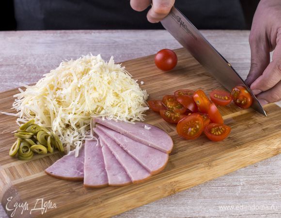 Нарежьте тонкими полосками ветчину. Натрите на крупной терке сыр. Порубите оливки колечками, а черри — кружками.
