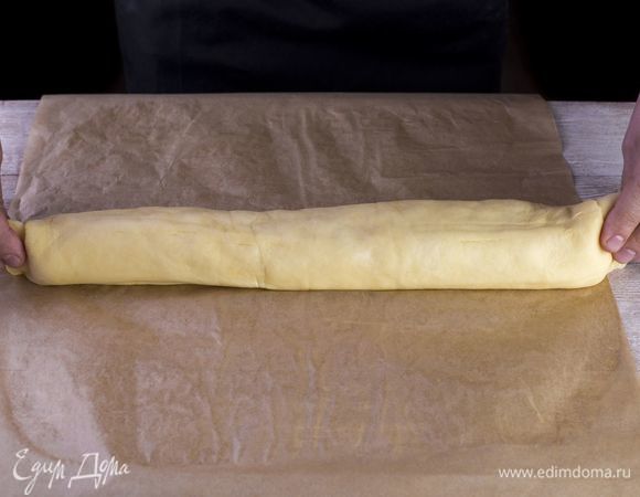 Сверните тесто с помощью пергамента в рулет.