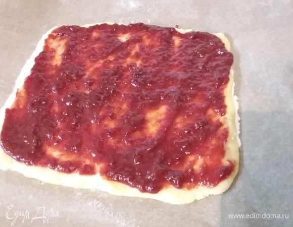 Один корж перенести на пергаменте на противень. Смазать малиновым вареньем.