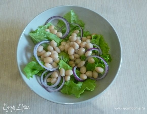 С фасоли ТМ «Фрау Марта» слить жидкость, добавить к салатным листьям. Лук нарезать тонкими кольцами.