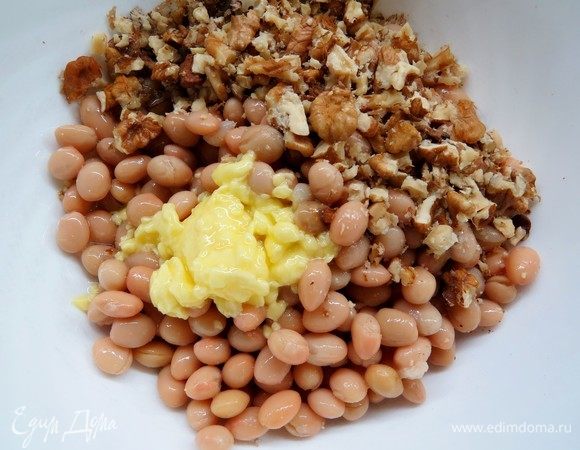 К фасоли добавить растопленное масло, половину рубленых орехов.