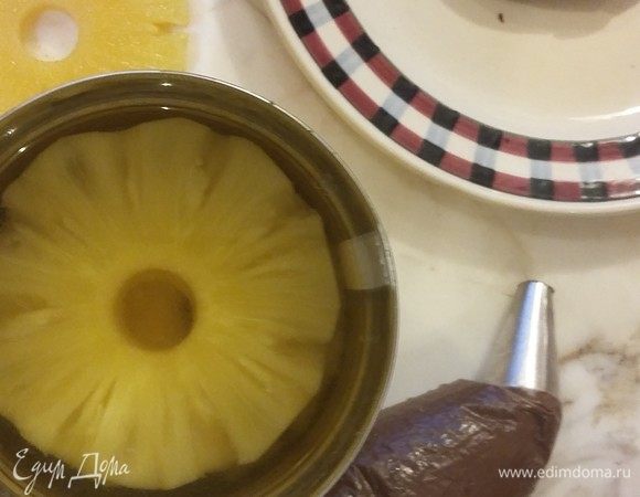 Приступаем к сборке. На первый корж намазываем крем и кладем кольцо ананаса ТМ «Фрау Марта», протертый бумажным полотенцем от лишней жидкости. Вдавливаем ананас в крем и закрываем вторым бисквитом. Промазываем кремом и выкладываем третий корж.