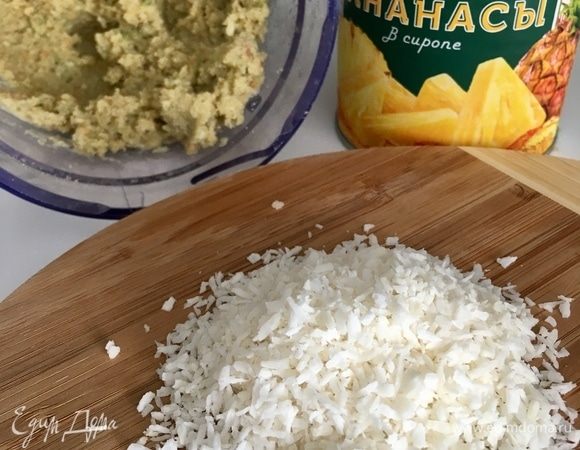 Берем припасенные кубики ананаса. На доску насыпаем кокосовую стружку. Бисквитная масса однородная и готова к работе.