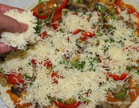 Сверху накройте пиццу натертым сыром и отправьте ее выпекаться в горячую печь до готовности.