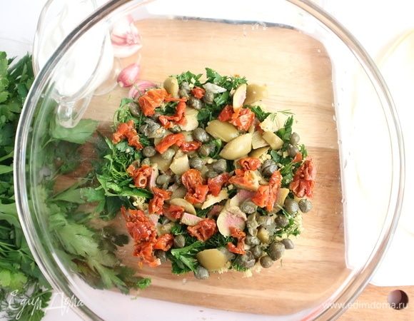 Удалить косточки из оливок. Одну оливку оставить для украшения. Добавить к зелени с чесноком нарезанные мелкими кусочками вяленые в масле томаты, маринованные каперсы, нарезанные на кусочки оливки.