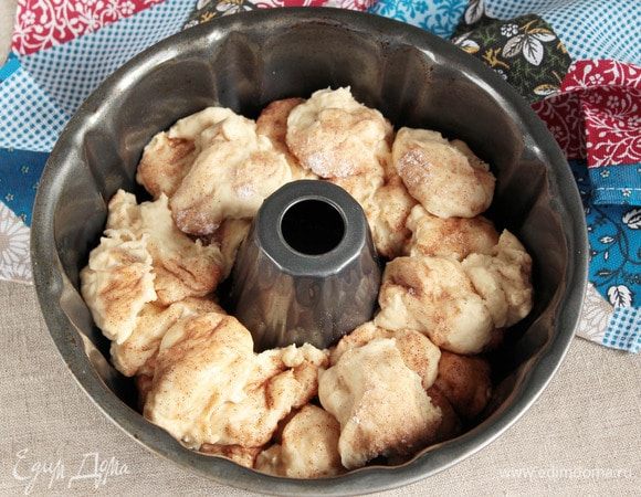 После того, как тесто увеличится в объеме, отщипывать кусочки размером с грецкий орех, и, не скатывая их, обваливаем со всех сторон в подготовленной сухой смеси. Полученные обваленные кусочки выложить в предварительно смазанную маслом растительным форму для выпечки (моя форма — 24 см в диаметре). Тесто никак специально не придавливать, но необходимо постараться как можно более равномерно по всей форме по принципу кладки кирпичей.