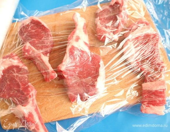 Кусочки корейки ягненка с косточкой положить на разделочную доску на некотором расстоянии друг от друга. Накрыть пищевой пленкой.