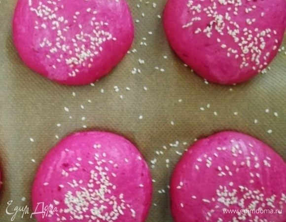 Выкладываем заготовки на противень, слегка придавливаем. Оставляем на расстойку на 15 минут, смазываем верх булочек водой и посыпаем кунжутом. Выпекаем в разогретой до 200°C духовке 15 минут.