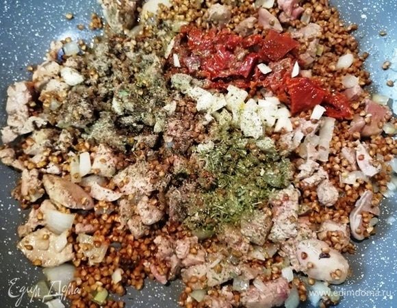 Всыпаем в сковородку гречу, добавляем специи (подойдут как для курицы, так и для мяса), чеснок, вяленые помидоры, соль и перец. Перемешиваем и оставляем подружиться все продукты буквально минуту.