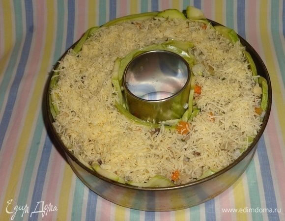 Выложить в кольцо с кабачками начинку, посыпать частью сыра. Сверху уложить оставшиеся пластины. Разъемную форму поставить в поддон (сковороду большего диаметра или противень). Духовку разогреть до 180°С, поставить форму с блюдом. Запекать в течение 1 часа. Вынуть из духовки, посыпать оставшимся сыром, поставить еще на 10 минут. Когда блюдо будет готово, можно просто убрать разъемную часть и поставить на блюдо. Я захотела выложить блюдо полностью из формы. Для этого я сначала убрала разъемную часть и поставила форму на плоское блюдо. Сверху накрыла другим плоским блюдом, а сверху большой глубокой миской. Перевернула блюдо «с ног на голову», вынула кольцо. Накрыла опять плоским блюдом и перевернула обратно. Как говорится, ловкость рук и никакого мошенничества. Если сами не справляетесь с этой задачей, позовите помощников, а то можно обжечься, ведь блюдо только из духовки.