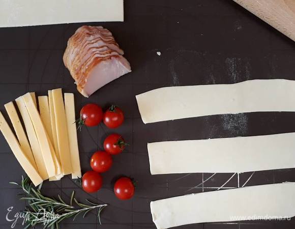 Слоеное тесто немного размораживаем и раскатываем, разрезаем на полоски шириной около 7 см.