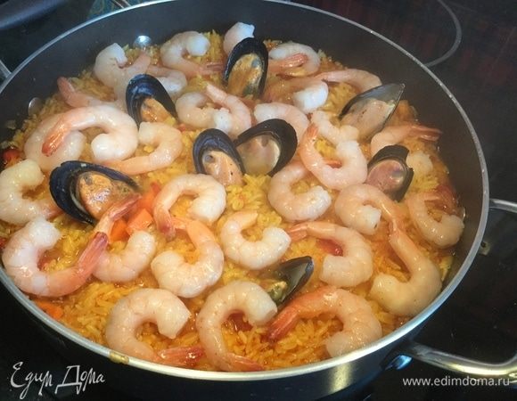 Аккуратно откройте крышку и выложите сверху креветки и мидии (замороженные), накройте крышкой, сделайте сильный огонь и готовьте 4 минуты, после чего выключите огонь и дайте паэлье настояться около 20 минут, крышку не открывайте.