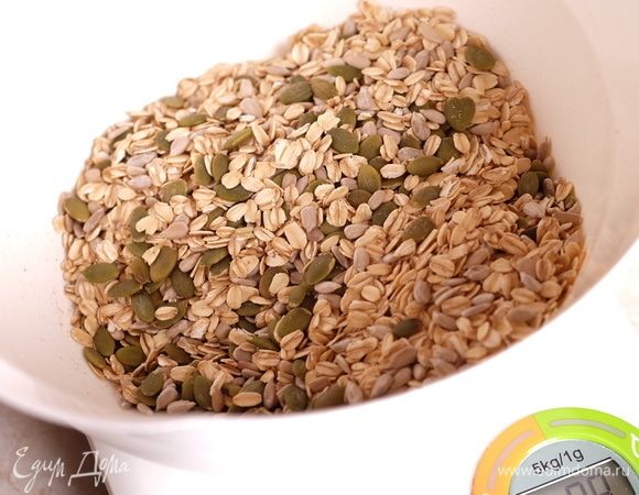 Духовку разогреть до 150°C. Желательно с камнем для выпечки. На нем гранола запечется особенно хорошо. В миске смешать овсяные хлопья, тыквенные семечки и семена подсолнуха.