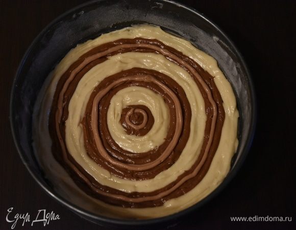 Форму для выпечки (диаметр — 20 см) смазать подсолнечным маслом, слегка присыпать мукой. Излишки муки стряхнуть. Выложить тесто кругами, чередуя белый цвет и темно-шоколадный. Поверх темного цвета нанести тонкую линию из светлого шоколадного теста. Закрыть эту линию слоем темного шоколадного теста.