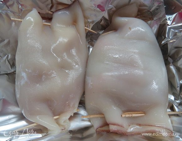 Форму выстелить фольгой, равномерно смазать 1 ст. л. оливкового масла, выложить нафаршированные тушки кальмара. Кальмары плотно закрыть фольгой и отправить в разогретую до 200°C духовку на 20 минут. За это время рыбка пропечется, станет сочной, а кальмар плотно обнимет ее.