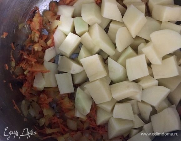 Как только лук стал прозрачным, а морковь мягче, добавляем в кастрюлю картофель, нарезанный кубиками. Перемешиваем, пару минут держим на огне и заливаем бульоном или бутилированной водой. Варить около 15 минут.
