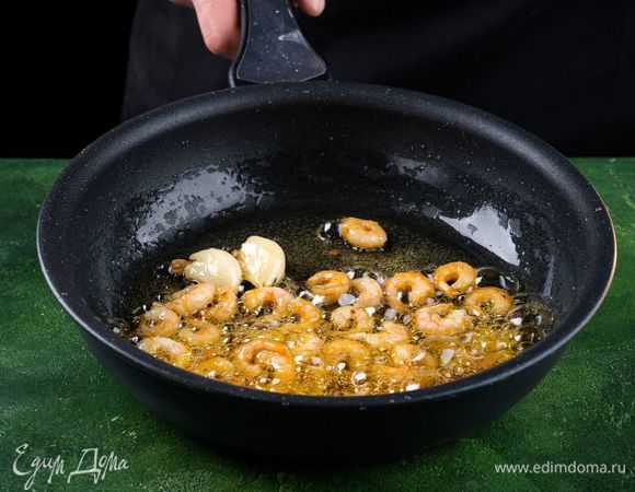 Разморозьте креветки и очистите их. В большой сковороде растопите 2 ст. л. сливочного масла и смешайте с 2 ст. л. оливкового масла. Добавьте измельченный чеснок и красный перец и обжарьте креветки приблизительно от 3 до 5 минут.