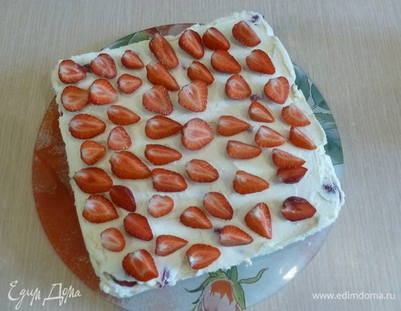 Оставшиеся ягоды разделить на 2 части, одну нарезать на половинки или четвертинки для украшения. Развернуть пленку, торт быстро перевернуть на вспомогательную тарелку или доску, удалить пленку. Перевернуть еще раз на блюдо для подачи. Разложить сверху нарезанную клубнику.