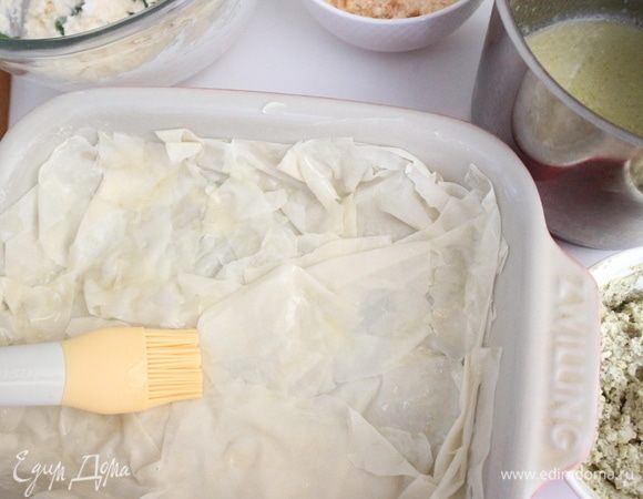 Духовку разогреть до 190°C. Форму немного смазать сливочным маслом, оставшуюся часть масла растопить. Дать остыть, добавить 4 ст. л. жидкости из упаковки с фетаксой, перемешать. В форму поместить несколько листиков теста фило, смоченных в миске со сливочным маслом и жидкостью из упаковки с фетаксой, сделать из теста складочки. Положить часть начинки из разных мисок, накрыть тестом фило, смоченном в этом же растворе.