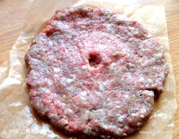Говяжий фарш смешать с солью, перцем и сформировать на квадратике пергамента лепешку, в центре сделать пальцем отверстие.