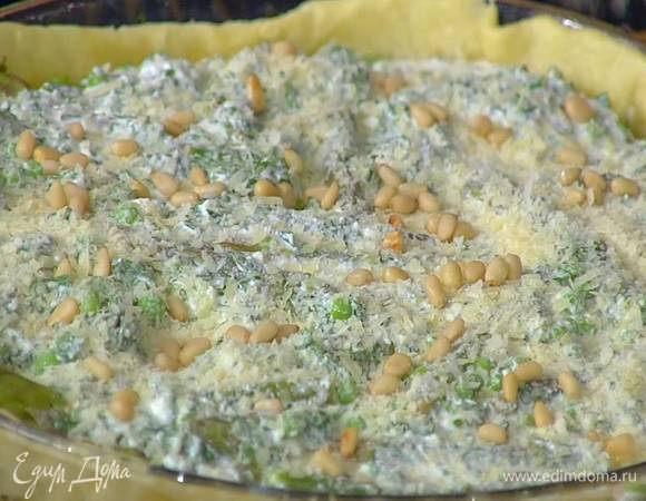 Подпеченное тесто в форме посыпать половиной оставшегося натертого сыра, разложить нарезанный лук, спаржу и зеленый горошек, залить все творожной массой с зеленью, посыпать оставшимся сыром и кедровыми орехами.