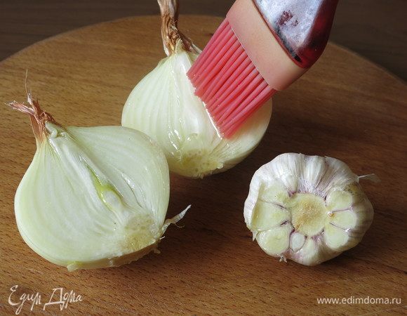 Лук нарезаем пополам, у чеснока срезаем донце и смазываем маслом.