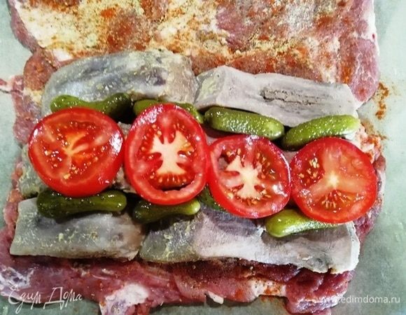 Разрезаем каждый язык вдоль пополам и выкладываем на свинину. Между языками укладываем маринованные корнишоны. Сверху выкладываем кольца помидора.