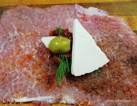 На каждую пластинку мяса в центр выкладываем 2 вяленых помидора черри, небольшую пластинку чеснока, половину маслины, укроп и половинку треугольника плавленого сыра.