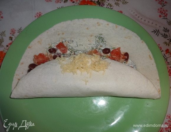 Загнуть один край тортильи на начинку, посыпать небольшим количеством сыра. Завернуть второй край лепешки внахлест на первый.