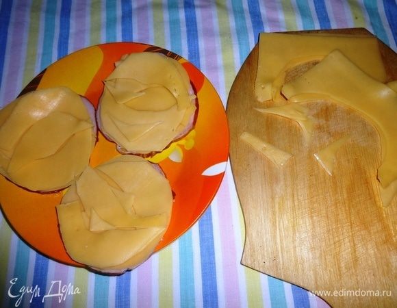 Уложить полукруги сыра на кружок карбонада. Так поступить со всеми кружками. Из оставшихся частей сыра вырезать различные округлые фигуры и также уложить их на кружки карбонада.