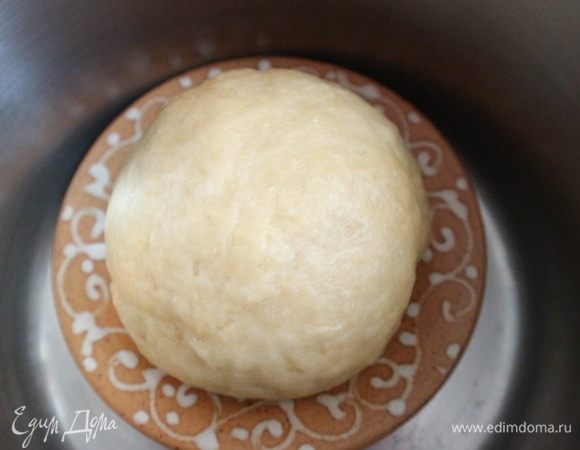 В большой теплоемкой кастрюле вскипятить воду. Вылить воду, на дно горячей сухой кастрюли поставить керамическое блюдце, на него положить тесто, закрыть крышкой кастрюлю и оставить на 30 минут. Можно просто накрыть тесто горячей кастрюлей.